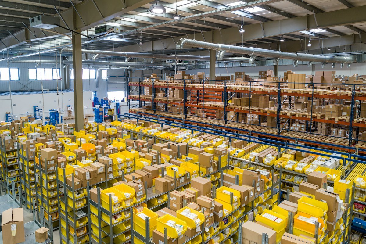 Yellow storage bins full of cartons on warehouse shelves, with larger boxes on the racks above
