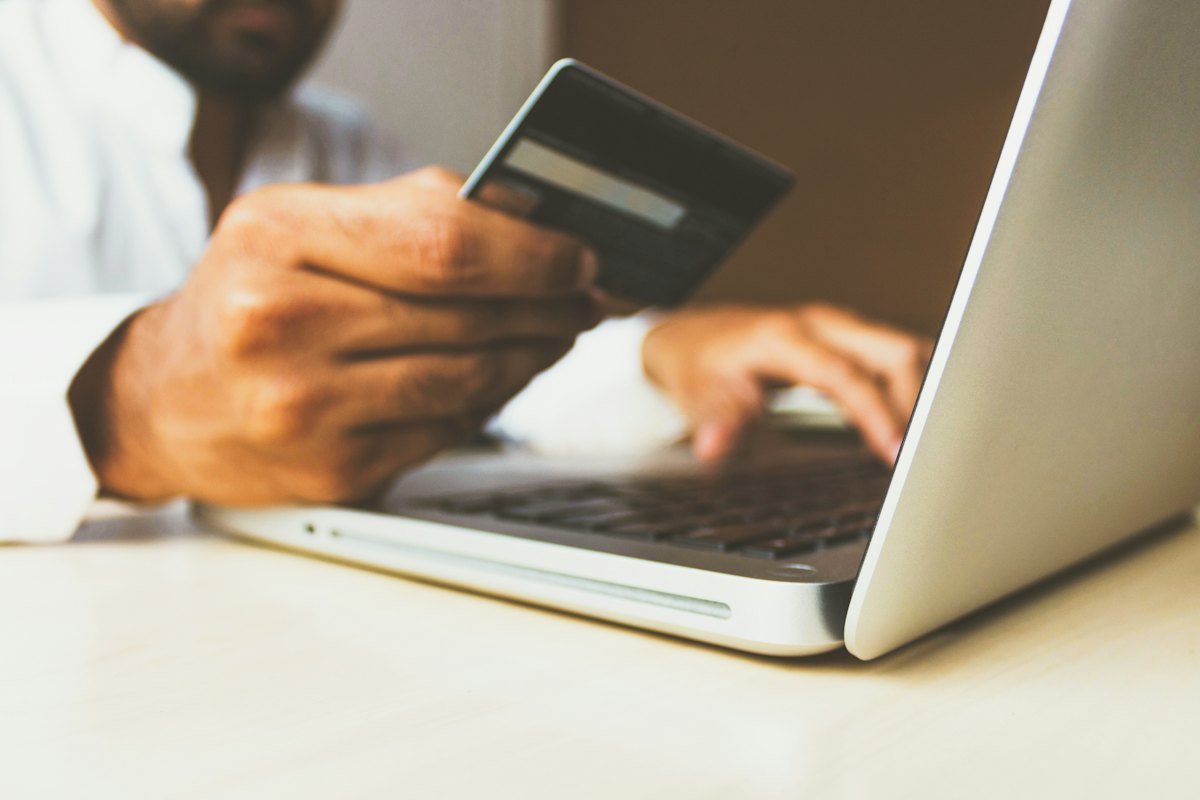A person holding a bank card next to an open laptop on a desk
